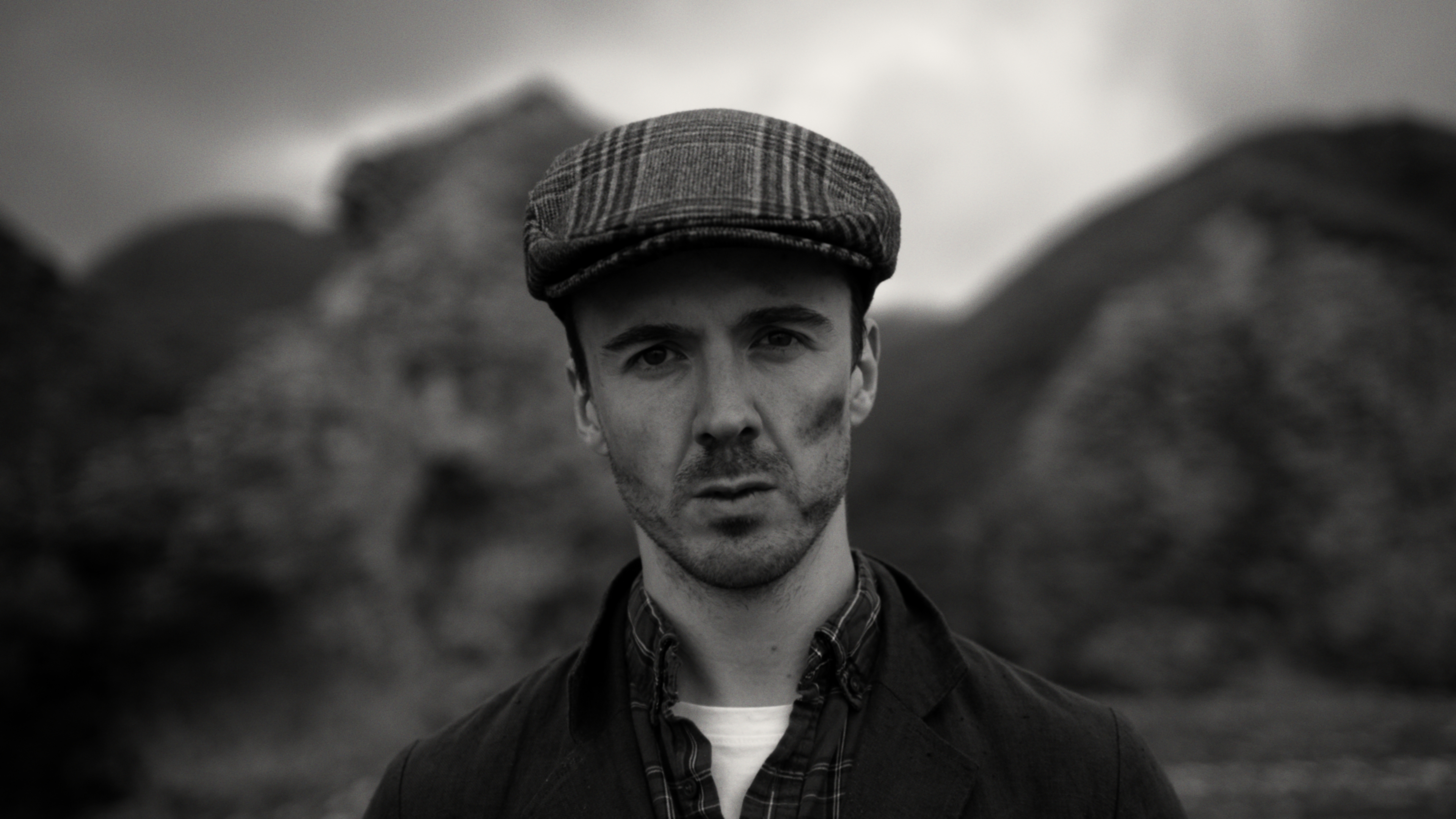 A young man wearing a flat cap with a coal stained face standing in a quarry