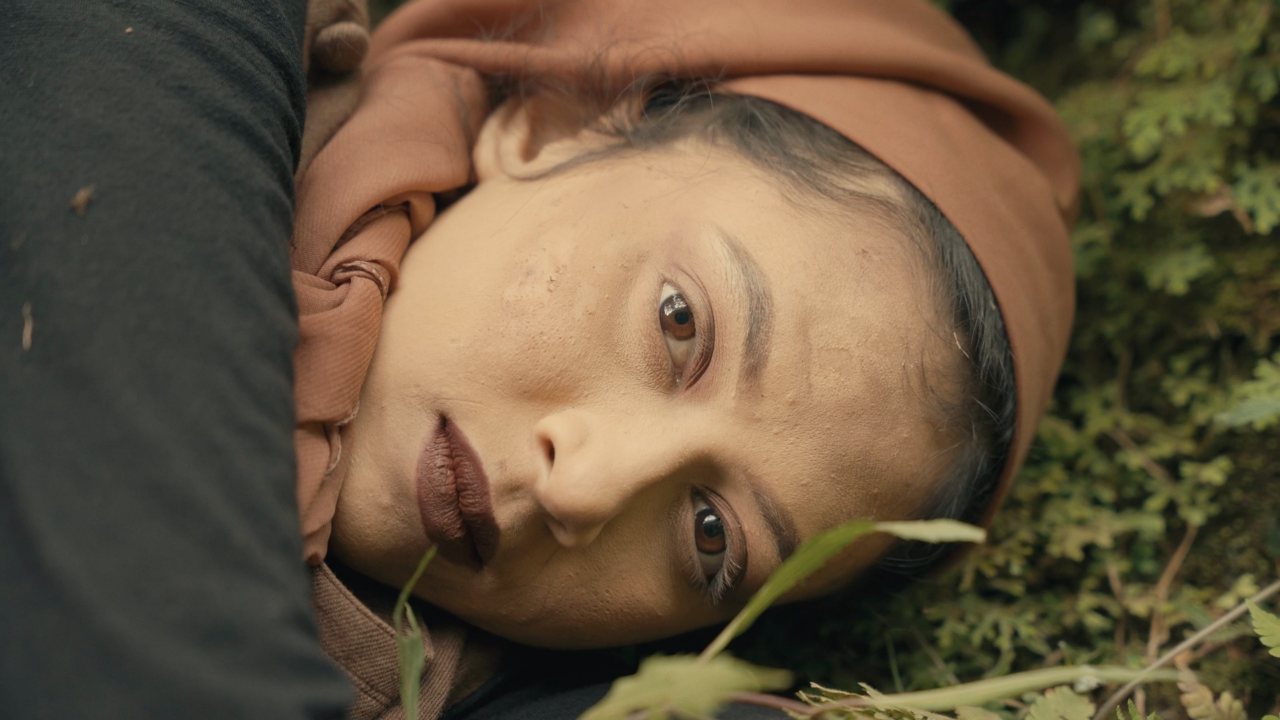 A video still of a woman lying down on the forest floor