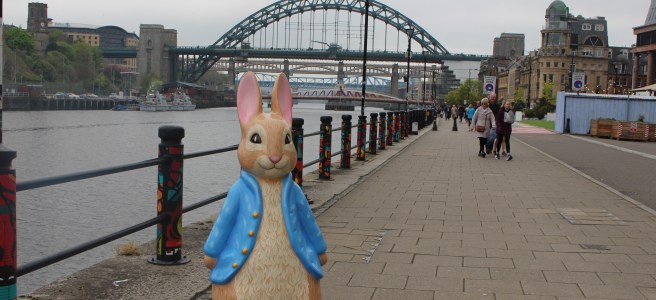 A statue of Peter Rabbit(TM) on Newcastle Quayside with the Tyne bridges behind him