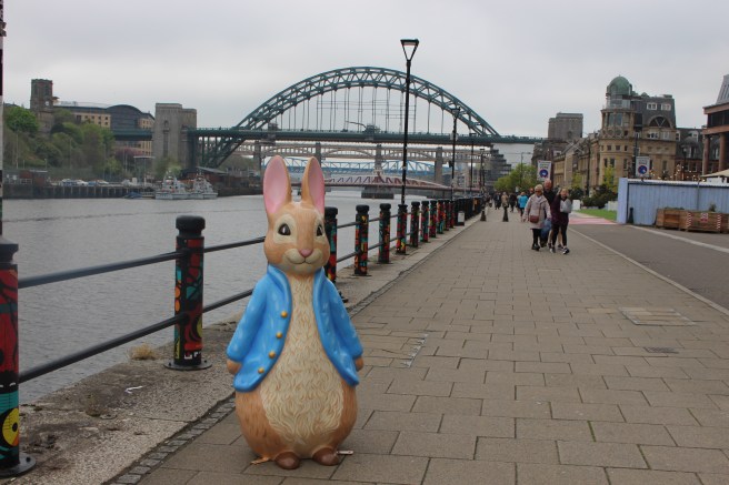 A statue of Peter Rabbit(TM) on Newcastle Quayside with the Tyne bridges behind him